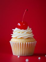 Vanilla cupcake with swirled buttercream frosting topped with glossy maraschino cherry against vibrant red background, perfect for dessert menus.