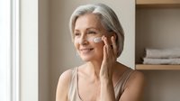 Mature woman applying face cream in bathroom, skincare routine for aging skin, anti-aging moisturizer application, senior beauty and wellness concept.