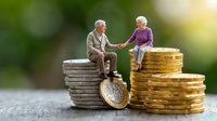 Senior couple figurines sitting on stacks of coins discussing retirement planning and financial security for elderly investment strategies.