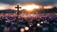 Cross silhouette against dramatic sunset sky with purple wildflowers in foreground, glowing bokeh lights create magical atmosphere in meadow at dusk.