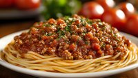 Delicious spaghetti pasta with rich meat sauce topped with fresh herbs on white plate. Classic Italian comfort food perfect for restaurant menus and cooking blogs.