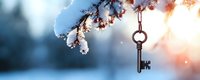 Vintage key hanging on snow-covered winter branch against blurred blue background with sunlight bokeh, creating magical seasonal atmosphere.