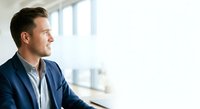 Caucasian male professional in navy blazer and light shirt gazing out bright office window, contemplative expression, suitable for corporate, business leadership, and career-related projects.