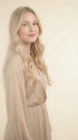 Young blonde Caucasian woman in beige dress smiling confidently against neutral background for lifestyle and fashion content.
