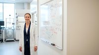 Professional businesswoman in white blazer standing confidently next to whiteboard with diagrams in modern office environment for corporate presentations.