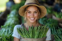 Young woman with fair skin and blonde hair wearing straw hat holding fresh asparagus bunch in garden setting for organic farming, agriculture, and healthy food concepts.