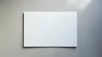 Blank white canvas or paper sheet mounted on gray textured wall with natural lighting and shadow effects for mockup presentations and design projects.