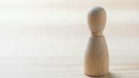 Single wooden bowling pin on light wood surface with soft natural lighting for sports and recreation concepts.