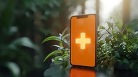 Smartphone with glowing medical cross symbol on orange screen surrounded by green plants in natural sunlight, representing digital healthcare solutions.