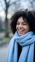 Happy young African American woman with curly hair wearing blue scarf laughing outdoors in winter park setting for lifestyle and wellness content.