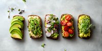 Variety of healthy open sandwiches with avocado, microgreens, radish, and cherry tomatoes on whole grain bread against light background.