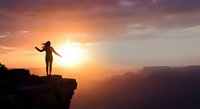 Woman silhouette standing on cliff edge with arms raised celebrating freedom at golden sunrise over mountain landscape for motivation and success.