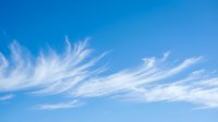 Wispy white cirrus clouds streak across bright blue sky creating natural patterns. Clear weather background for outdoor activities and seasonal designs.