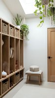 Modern mudroom interior with wooden storage cubbies, wicker baskets, hanging plants and natural skylight for organized home entryway design.