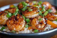 Glazed honey garlic shrimp served over steamed white rice and garnished with fresh chopped green onions, close up view of Asian fusion cuisine dish.