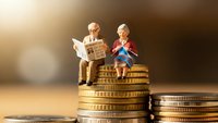 Miniature elderly couple sitting on stack of golden coins representing retirement savings and financial planning for senior years.