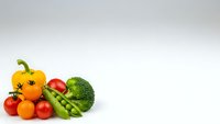 Fresh organic vegetables including yellow bell pepper, cherry tomatoes, peas and broccoli arranged on white background for healthy cooking and nutrition.
