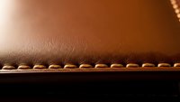 Brown leather material with decorative stitching edge detail for luxury craftsmanship and premium quality goods manufacturing backgrounds.