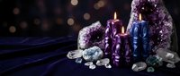 Mystical crystal healing setup with amethyst geodes, colorful candles and gemstones on dark velvet fabric creating spiritual meditation atmosphere.