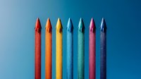 Vibrant colored pencils arranged in rainbow order against blue background, standing vertically in minimalist composition. Clean professional photo for education and creativity concepts.