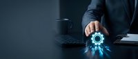 Businessman in suit holding glowing gear icon on dark desk with coffee cup and tablet, representing digital technology, innovation, and business solutions.