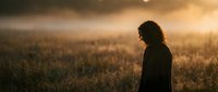 Young woman with curly hair standing in golden wheat field during sunset, silhouette against warm light, peaceful rural landscape, agriculture concept.
