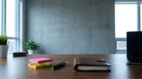 Minimalist workspace with wooden desk, notebook, pen, sticky notes, potted plants, and concrete wall backdrop for office design projects.