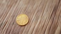 Golden ancient coin on wooden surface with diagonal lines pattern, shallow depth of field creates soft blurred background for financial concepts.