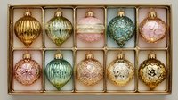 Elegant collection of vintage-style Christmas ornaments in pastel colors with gold accents arranged in decorative box, perfect for holiday decor.