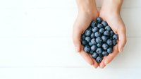 Caucasian hands holding fresh blueberries on white background, overhead view. Use for food, nutrition, healthy eating, and wellness content.