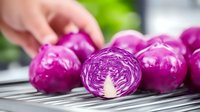 Fresh purple cabbage being sliced on kitchen counter, showing vibrant cross-section layers. Healthy cooking preparation for salads and meals.