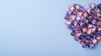 Small metallic pink and purple hearts arranged in heart shape on light blue background. Romantic composition for Valentine's Day cards and love messages.