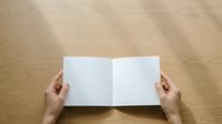 Open blank magazine or brochure mockup held by hands against neutral beige background, suitable for design presentations and marketing materials.