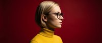 Professional blonde woman in yellow turtleneck and glasses against red background for corporate branding and business presentations.