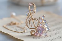 Delicate gold treble clef pendant with pink and crystal gemstones on vintage sheet music background, elegant musical jewelry accessory for musicians and music lovers.