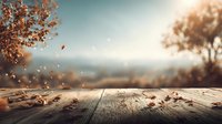 Rustic wooden table with autumn leaves against blurred fall landscape background with golden foliage and soft sunlight.
