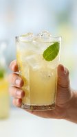 Hand holding refreshing lemonade with mint garnish and ice cubes in glass on bright summer day for beverage and hospitality concepts.