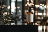 Amber glass bottle with blank label against blurred Christmas tree and bokeh lights background, creating luxurious festive mood for cosmetic product photography.