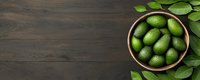 Fresh green avocados in wooden bowl with leaves on dark rustic wooden background, top view with copy space for food banner design.