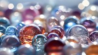 Colorful glass marbles in vibrant blue, red, orange, and purple tones with soft bokeh effect creating dreamy atmosphere for decorative backgrounds.