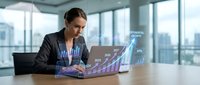 Young Asian businesswoman working on laptop with glowing holographic financial growth charts and KPI data projections in modern office.
