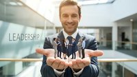 Smiling Caucasian businessman in suit holding miniature business people figures in office, representing team leadership and human resources management.