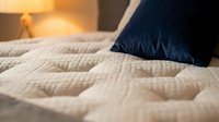 Comfortable bed with quilted white mattress and dark blue pillow, warm bedroom lighting in background, cozy sleeping environment for home decor and lifestyle content.