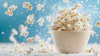 Fresh popcorn kernels floating and falling into white ceramic bowl against blue background with dynamic motion and salt particles in bright lighting.