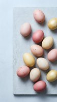 Pastel Easter eggs in pink, yellow, and beige tones arranged on a marble stone slab against a light gray background.