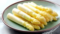 Fresh white asparagus spears arranged on green ceramic plate with red rim, showcasing seasonal spring vegetables for food photography and culinary presentation.