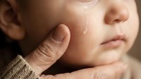 Gentle adult hand touching soft cheek of peaceful sleeping newborn baby with tender care and love in warm natural light creating intimate bonding moment.