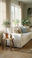 Bright modern living room with white sofa, houseplants, wooden stool and natural light streaming through large windows creating cozy Scandinavian interior.
