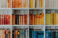 Colorful vintage books arranged by color on white bookshelf, creating rainbow spectrum from red to yellow to blue tones.