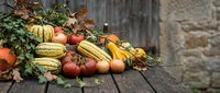 Autumn harvest display with pumpkins, gourds, tomatoes and fall leaves arranged on rustic wooden table for seasonal decoration and thanksgiving celebration.